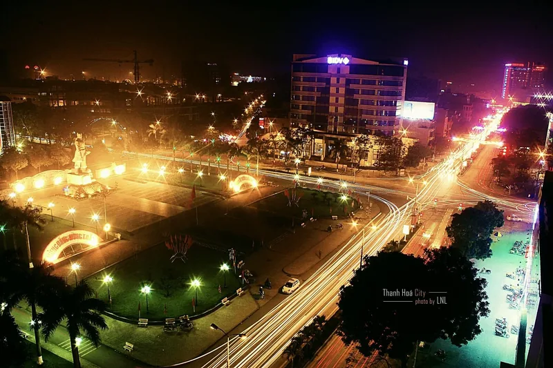 Toàn cảnh thành phố Thanh Hóa về đêm với vòng xoay sáng đèn, tượng đài và vệt đèn xe cộ.