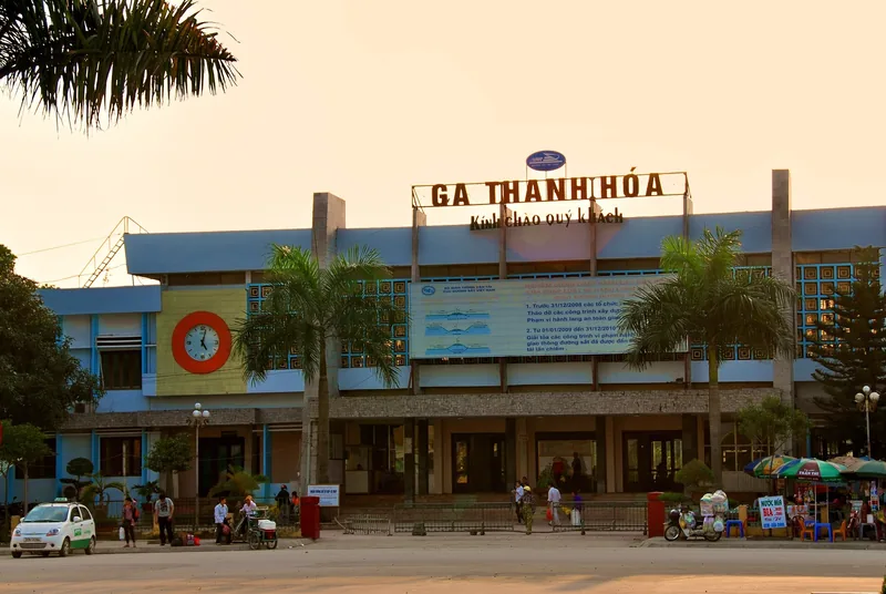 Mặt tiền ga Thanh Hóa ở Việt Nam lúc chiều tối, với hàng cọ và người bán hàng bên ngoài.