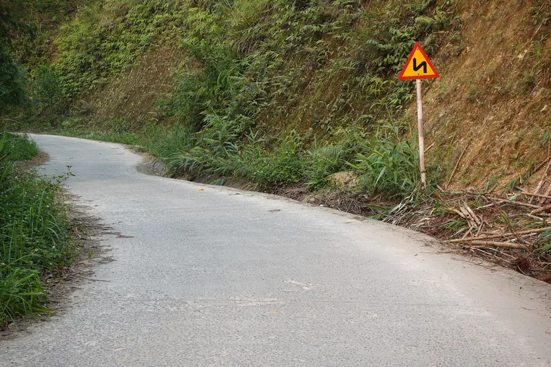 Con đường nông thôn uốn lượn với biển báo cong xuyên qua sườn đồi xanh ở Pù Luông.